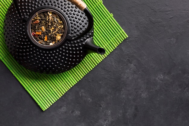 Erhöhte Ansicht der schwarzen Teekanne mit getrocknetem Teekraut auf grünem Tischset