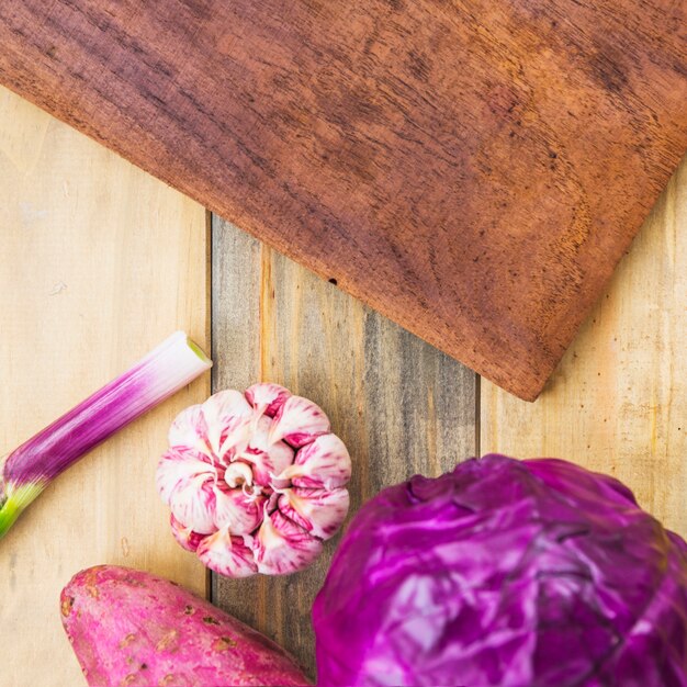 Erhöhte Ansicht der Süßkartoffel; Knoblauch und Purpurkohl und Schneidebrett auf hölzernen Hintergrund