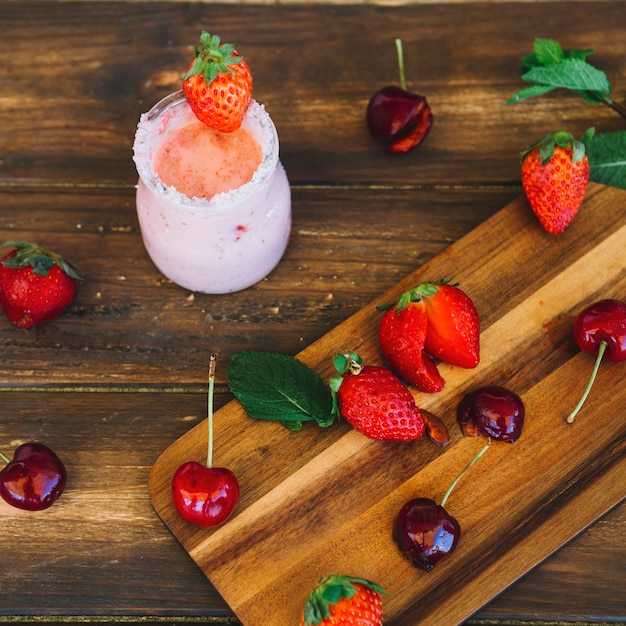 Erhöhte Ansicht des frischen Smoothie nahe Kirschen und der Erdbeeren auf Schneidebrett