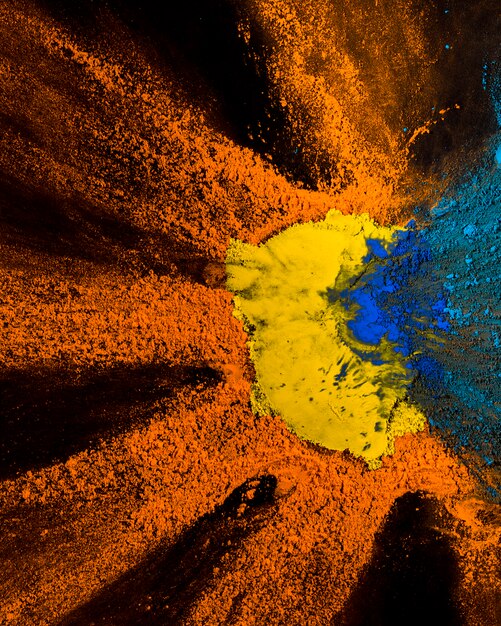 Erhöhte Ansicht des gelben, orange und blauen holi Pulverdesigns auf schwarzem Hintergrund