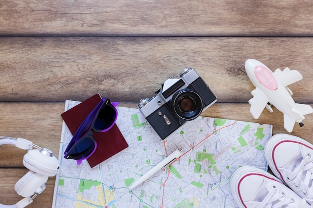 Erhöhte Ansicht des Kopfhörers; Reisepass; Sonnenbrille; Karte; Stift; Kamera; Schuhe und Flugzeug auf hölzernen Hintergrund