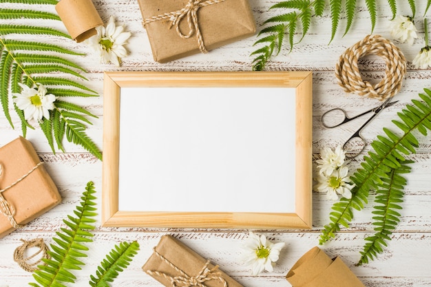 Erhöhte Ansicht des leeren Rahmens umgeben von Geschenken; Blätter und weiße Blüten