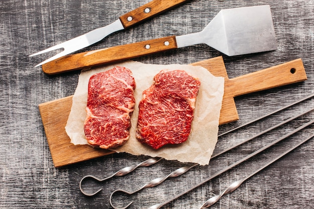 Erhöhte Ansicht des rohen Steaks und des Grillgeräts auf hölzerner strukturierter Oberfläche