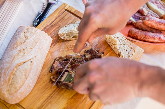 Erhöhte Ansicht einer menschlichen Hand, die gekochtes Fleisch auf hölzernem hackendem Brett schneidet