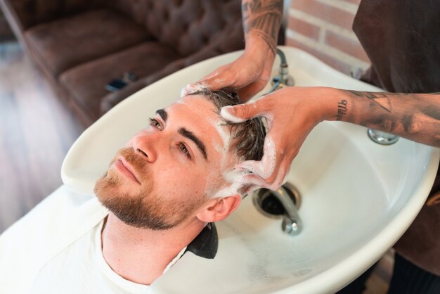 Erhöhte Ansicht eines Friseurs mit Tätowierungen, die die Haare eines jungen männlichen Kunden waschen