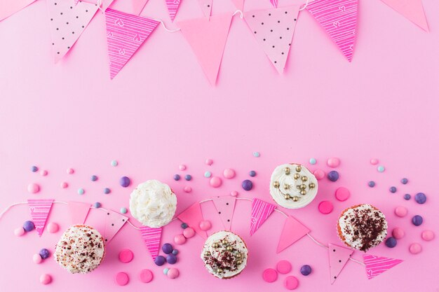 Erhöhte Ansicht von Cupcakes; Süßigkeiten und Flagge auf rosa Hintergrund