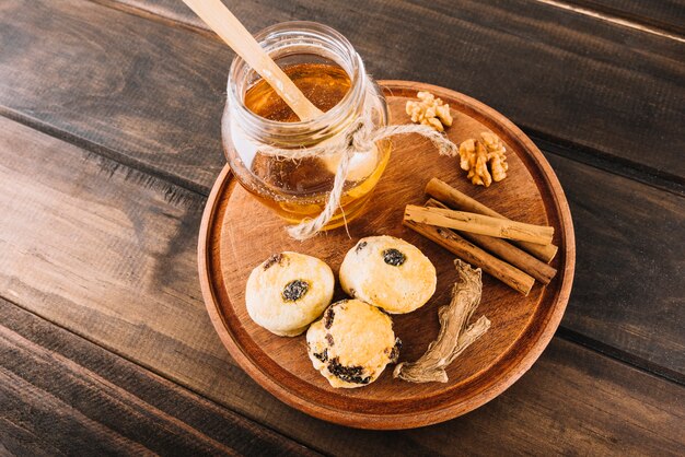 Erhöhte Ansicht von Honig; Nussbaum; Zimt; Tasse Kuchen und Ingwer auf Holzbrett