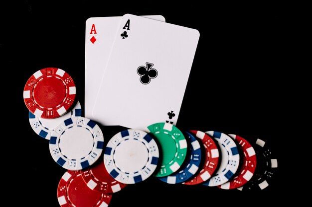 Erhöhte Ansicht von Pokerchips und zwei Spielkarten mit Assen auf schwarzem Hintergrund