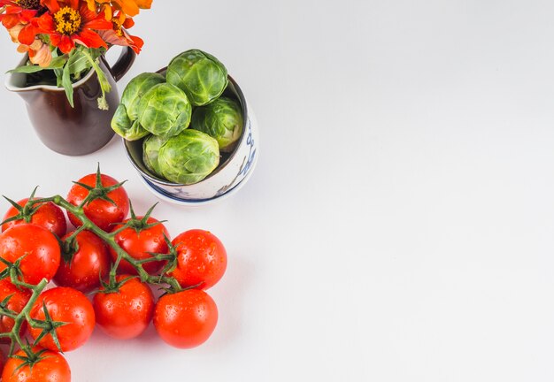 Erhöhte Ansicht von saftigen Tomaten; Rosenkohl und Blumen auf weißem Hintergrund