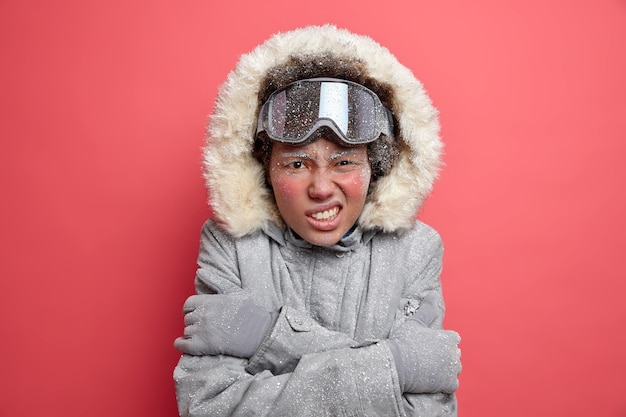 Erholungs- und aktives Freizeitkonzept. Unzufriedene Frau beißt die Zähne zusammen und umarmt sich, da sie im frostigen Januar sehr kalt zittert. Im Winter trägt sie warme Kleidung für kaltes Wetter