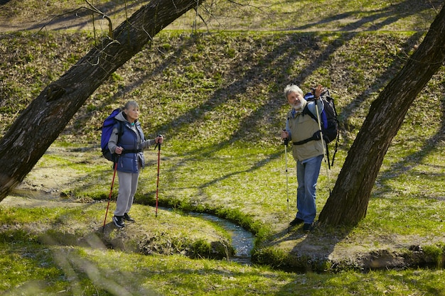 Erinnerungen an das Glück. Alter Familienpaar von Mann und Frau im Touristenoutfit, das an grünem Rasen in sonnigem Tag nahe Bach geht