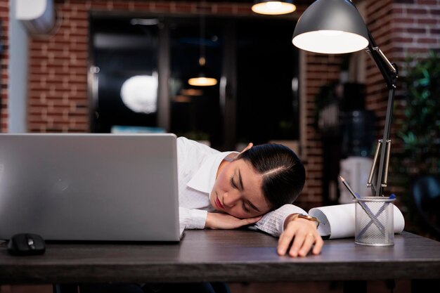 Ermüdeter Mitarbeiter eines Unternehmens, der wegen Überstunden in der Nacht auf dem Schreibtisch schläft. Erschöpfter Agenturangestellter schläft im Büroarbeitsplatz ein, während er an einem Projekt arbeitet.