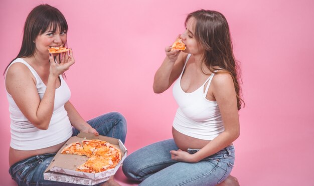 Ernährungskonzept, schwangere Frauen, die Pizza auf einer rosa Wand essen