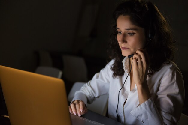 Ernste Frau mit Kopfhörer unter Verwendung des Laptops