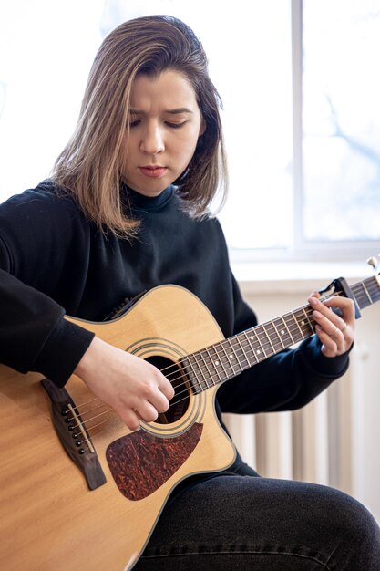 Ernste junge Frau, die zu Hause Akustikgitarre spielt