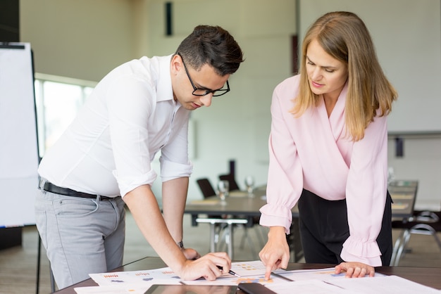 Ernste männliche und weibliche Kollegen, die mit Statistikdokumenten arbeiten.