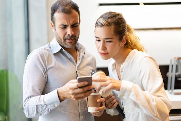 Ernste männliche und weibliche Kollegen, die Mitteilung auf Mobiltelefon lesen