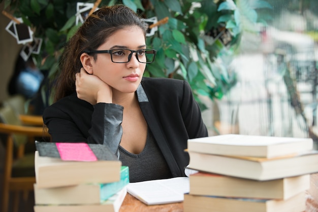 Ernste studentin sitzt am tisch mit bücher