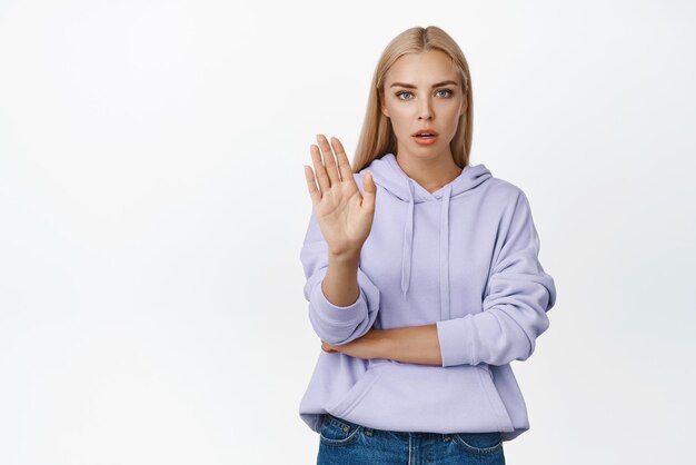 Ernste und selbstbewusste Frau widersprechen ausdrücklich dem Zeigen einer Stopp-Ablehnungsgeste, die besagt, dass sie nicht auf weißem Hintergrund stehen