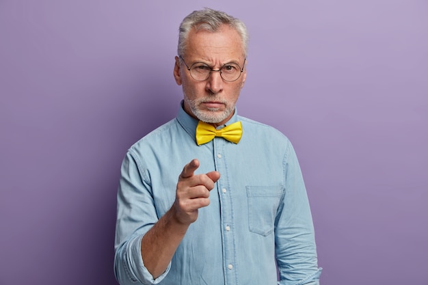 Kostenloses Foto ernster älterer mann im eleganten hemd mit gelber fliege, unzufrieden mit der unproduktiven arbeit der kollegen