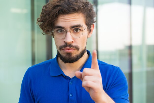 Ernster betroffener Kerl, der oben Zeigefinger zeigt