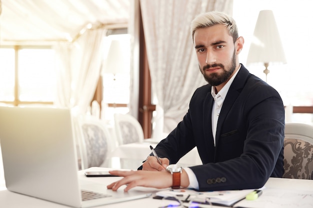 Ernster Chef schaut gerade und bereitet sich auf ein Geschäftstreffen mit einem Laptop im Restaurant vor