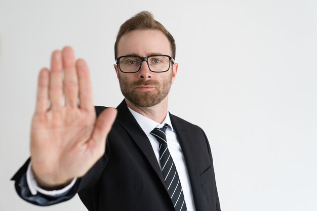 Ernster Geschäftsmann, der offene Palme oder Endgeste zeigt und Kamera betrachtet.