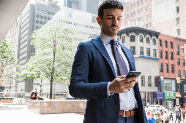 Ernster Geschäftsmann, der Smartphone auf Straße verwendet