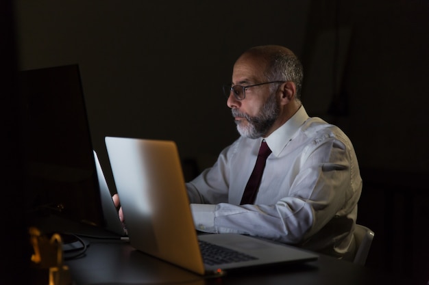 Ernster Geschäftsmann, der spät mit Laptop nachts arbeitet