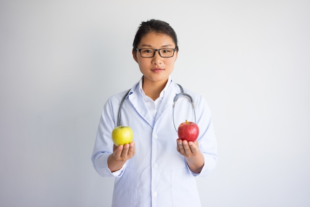 Ernster hübscher asiatischer weiblicher Doktor mit rotem und gelbem Apfel.