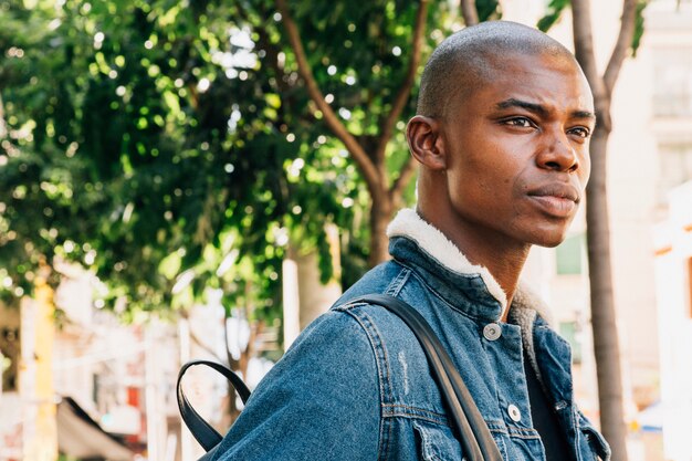 Ernster junger afrikanischer Mann mit Rucksack auf seiner Schulter, die weg schaut