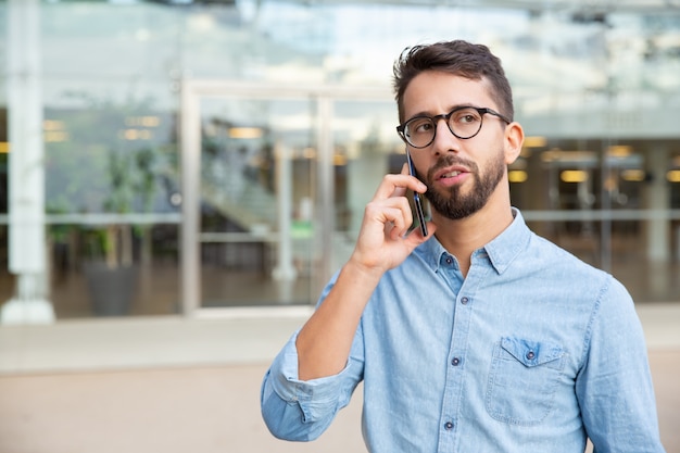 Ernster junger Mann, der durch Smartphone spricht