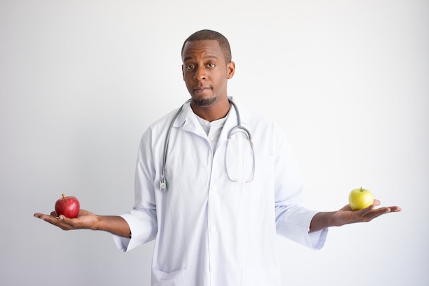 Ernster junger schwarzer männlicher Doktor, der die grünen und roten Äpfel hält.