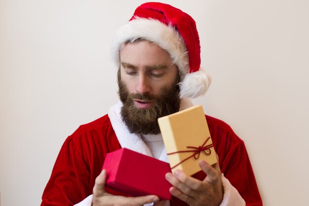 Ernster Kerl, der Sankt-Kostüm trägt und Geschenkbox untersucht