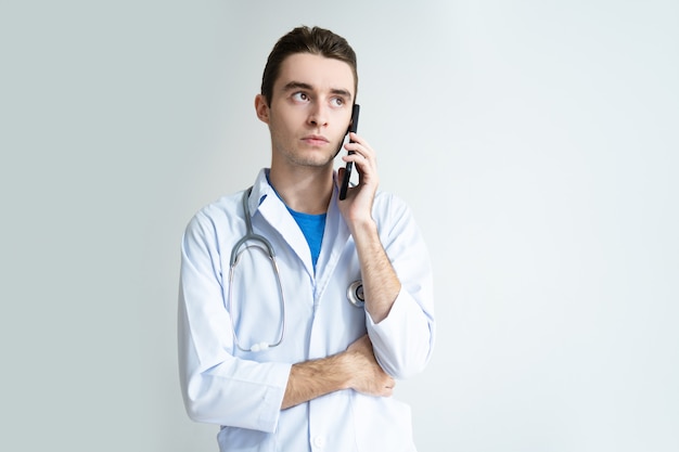 Ernster männlicher Doktor, der auf Smartphone spricht