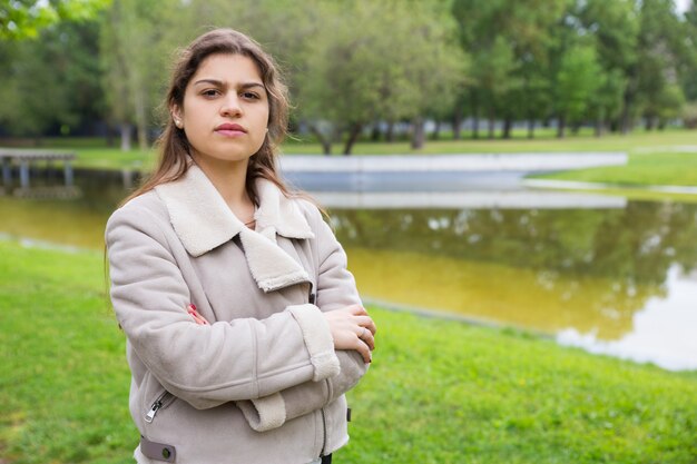 Ernstes Studentenmädchen, das im Park nahe Teich aufwirft