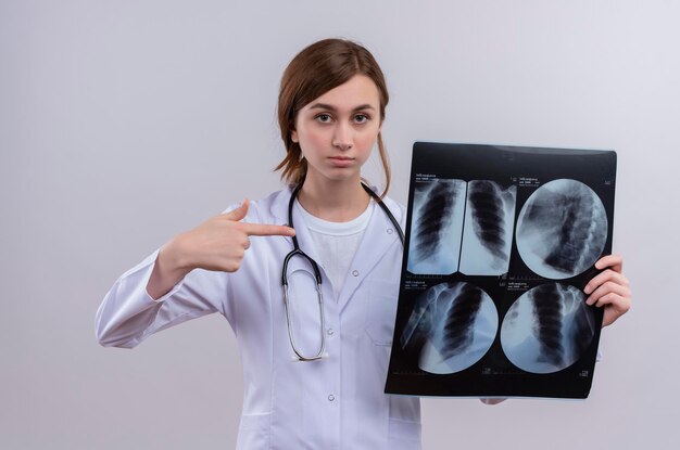 Ernsthaft aussehende junge Ärztin, die medizinische Robe und Stethoskop trägt und Röntgenaufnahme hält, die darauf zeigt