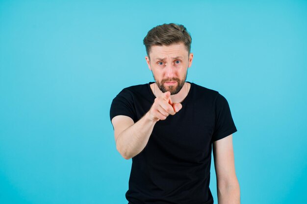 Ernsthaft betrachtet der Mann die Kamera, indem er den Zeigefinger auf blauem Hintergrund zur Kamera streckt