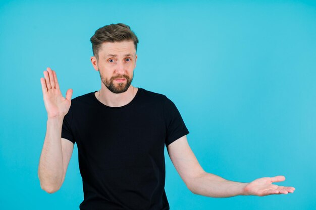 Ernsthaft hebt der Mann eine Hand und zeigt mit der anderen auf blauem Hintergrund nach rechts