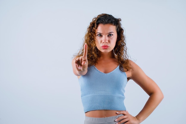 Kostenloses Foto ernsthaft, mädchen schaut in die kamera, indem sie eine winzige geste zeigt und die andere hand auf die taille auf weißem hintergrund legt