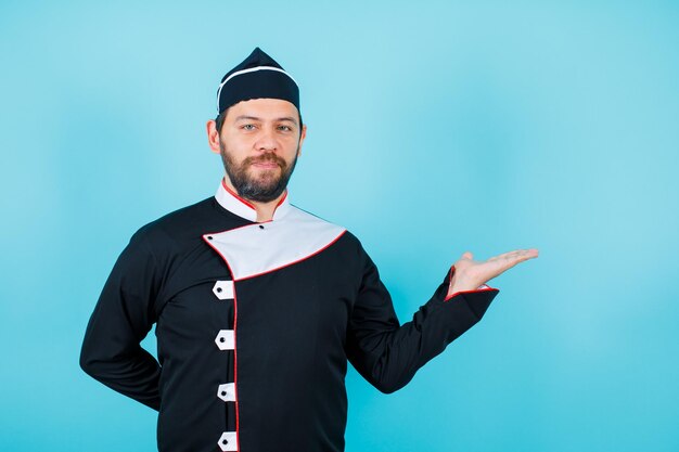 Ernsthaft zeigt der Koch mit der Hand nach rechts und legt die andere Hand auf den blauen Hintergrund
