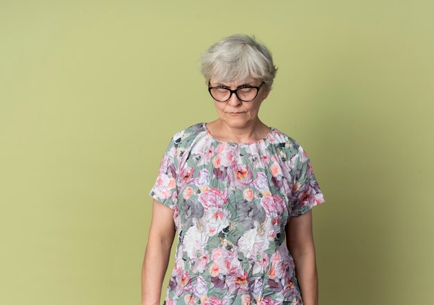 Ernsthafte ältere Frau in optischen Gläsern sieht isoliert auf olivgrüner Wand aus