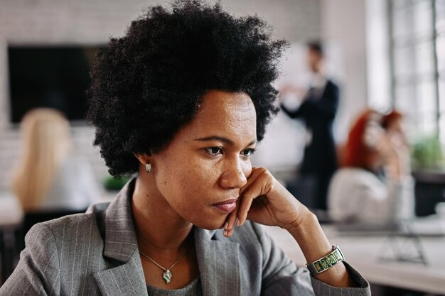 Ernsthafte afroamerikanische Geschäftsfrau, die an etwas denkt, während sie im Büro ist