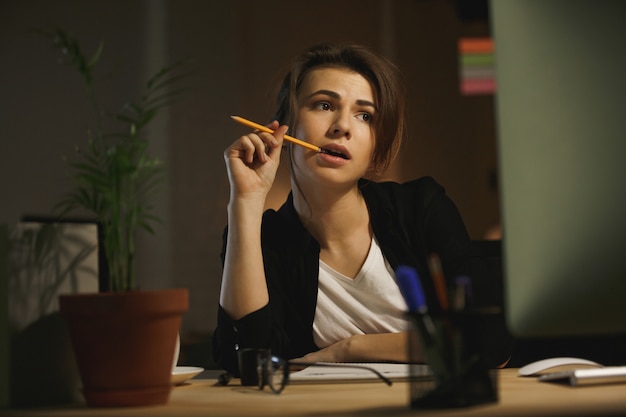 Ernsthafte junge Designerin, die nachts im Büro sitzt