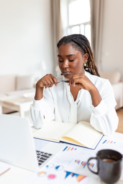 Ernsthafte, stirnrunzelnde afroamerikanische Ethnizität Frau sitzt am Schreibtisch am Arbeitsplatz schaut auf den Laptop-Bildschirm und liest E-Mails