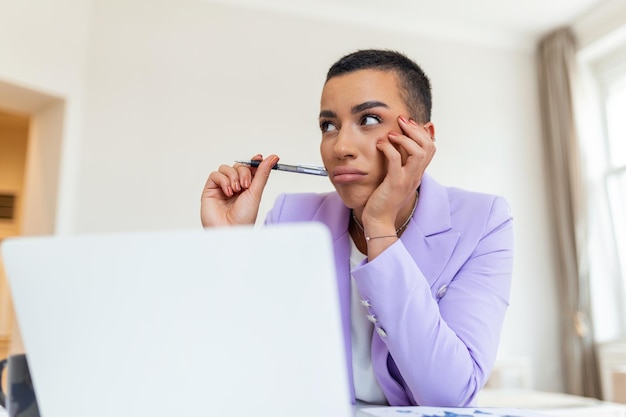 Ernsthafte, stirnrunzelnde afroamerikanische Ethnizität Frau sitzt am Schreibtisch am Arbeitsplatz schaut auf den Laptop-Bildschirm und liest E-Mails