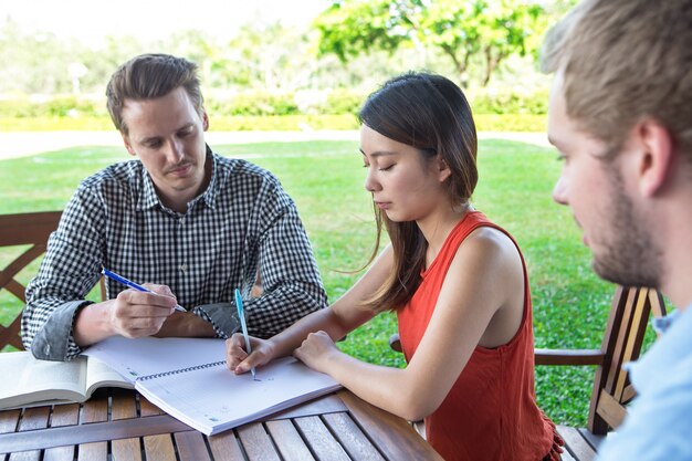 Ernsthafte Studentenfreunde machen Hausaufgaben im Freien