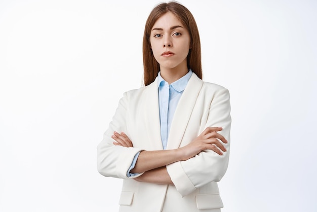 Ernsthafte und selbstbewusste, berufstätige Frau im Business-Anzug mit gekreuzten Armen auf der Brust sieht entschlossen aus mit selbstbewusstem Gesichtsausdruck auf weißem Hintergrund