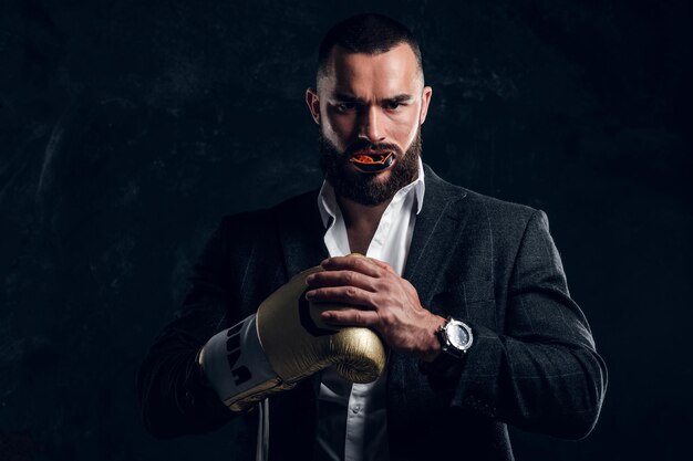 Ernsthafter brutaler Mann in Anzug und goldenem Boxhandschuh posiert für Fotografen im dunklen Fotostudio.