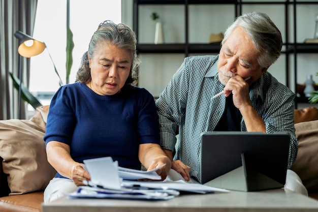 Ernsthaftes gestresstes asiatisches älteres altes ehepaar, das sich sorgen um rechnungen macht, bespricht unbezahlte bankschuldenpapiere traurige arme familie im ruhestand, die sich sorgen um geldprobleme macht